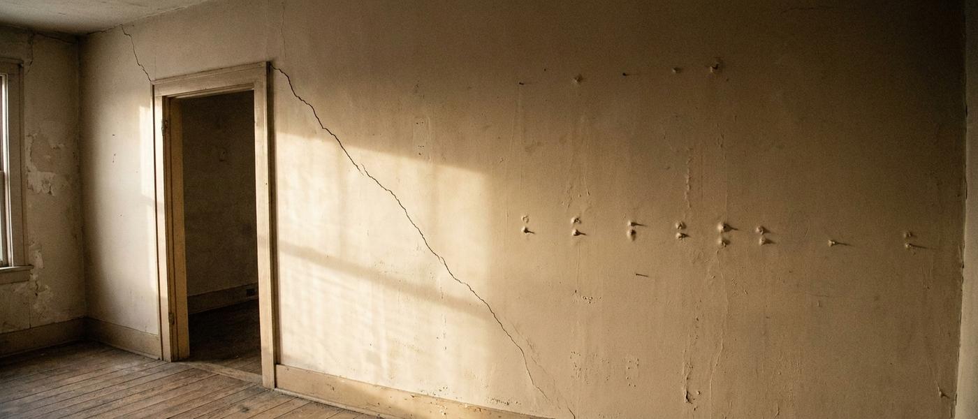 A diagonal settlement crack running from a door corner across an interior wall, with popped nail heads further along